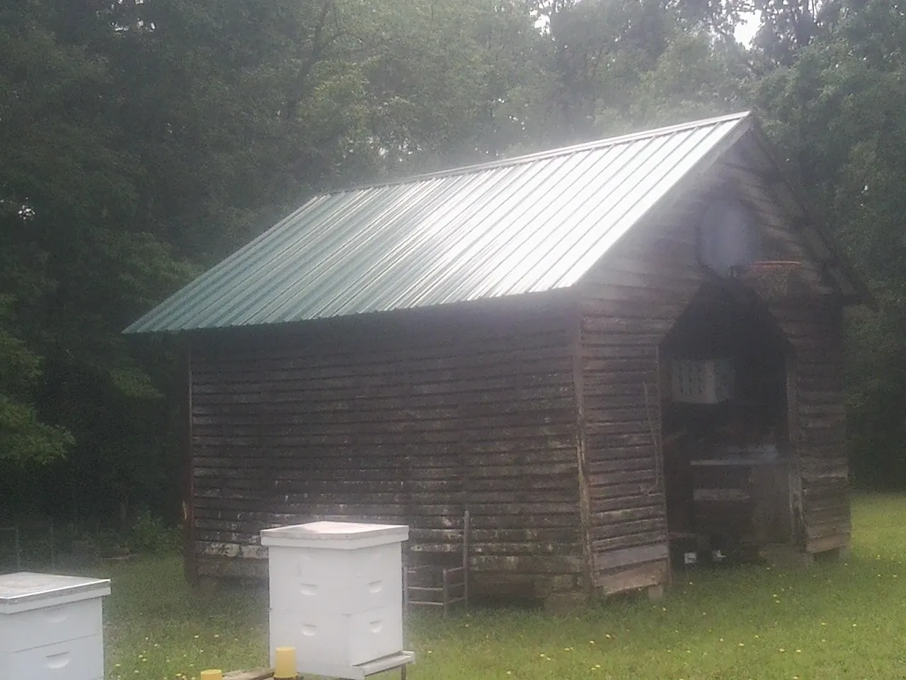 Green metal roof on a weathered barn beside stacked beehives in Trenton